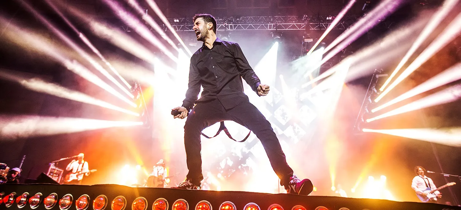 Melendi en el escenario, de negro, entre haces de luz blanca